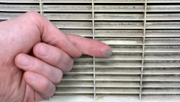 Person wiping finer across a dirt air vent, with dust visible on finger.