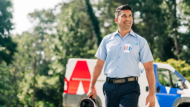 An asv technician walking upto a house holding a toolbag.