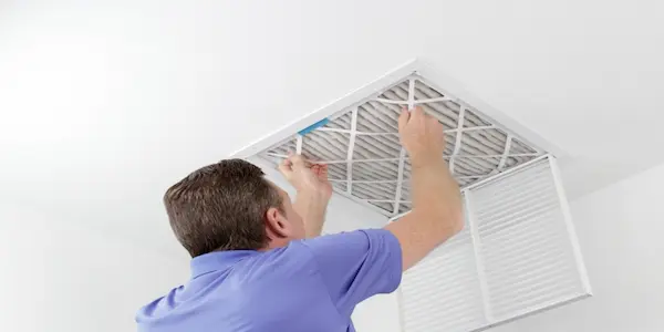 Man removing square, pleated and dirty air filter from AC vent in ceiling.