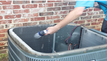 Man cleaning AC condenser coils with a hose.