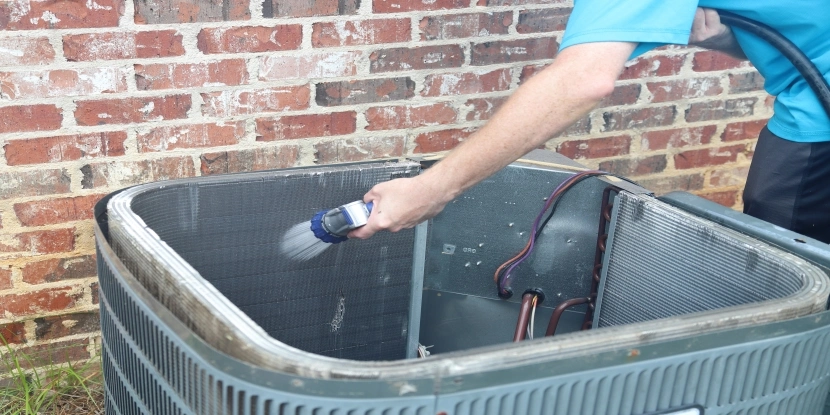 Man cleaning AC condenser coils with a hose.