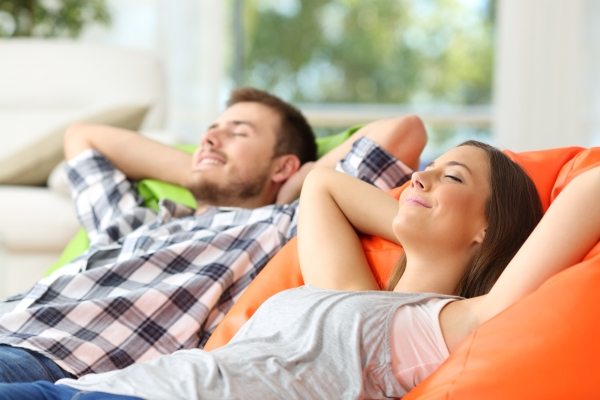 Young couple with arms folded behind their head resting comfortably on couch with eyes closed