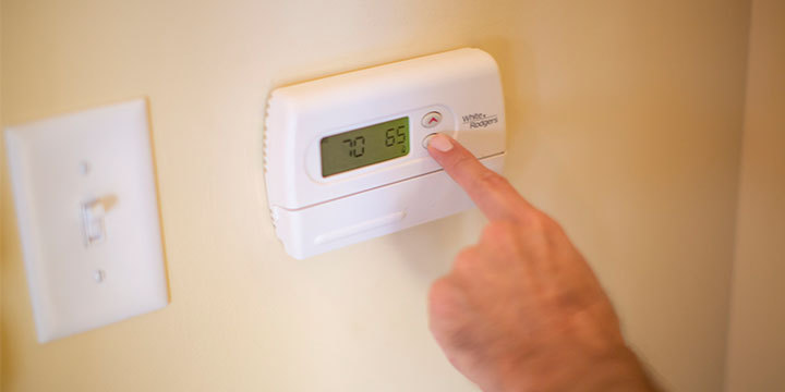 Hand turning down temperature on a digital thermometer on a yellow wall